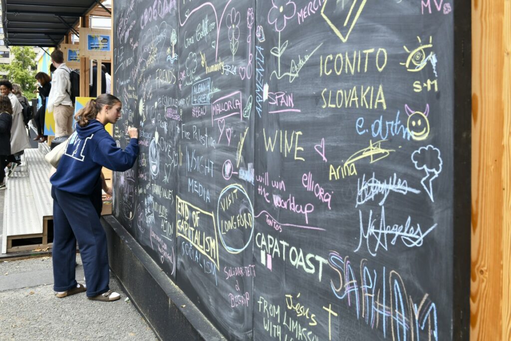 A young woman signing her name on the interactive wall at the FEST during NEB 2026